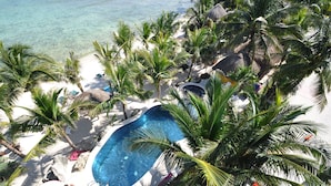 A pool surrounded by palm trees and rocks on a white sandy beach. - Absolute Beachfront - 3 Bedroom Condominium at Del Sol (Akumal)