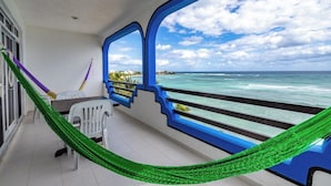 A balcony with a view of the ocean, a hammock, and a table with chairs. - Absolute Beachfront - 3 Bedroom Condominium at Del Sol (Akumal)