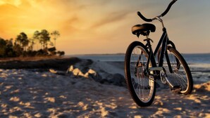 En cykel parkerad på en sandstrand med en solnedgång i bakgrunden.