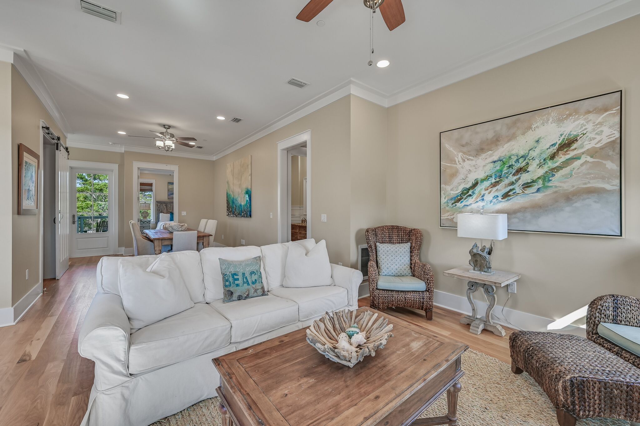 A spacious living room with a white sofa, a wooden coffee table, and a large abstract painting on the wall.