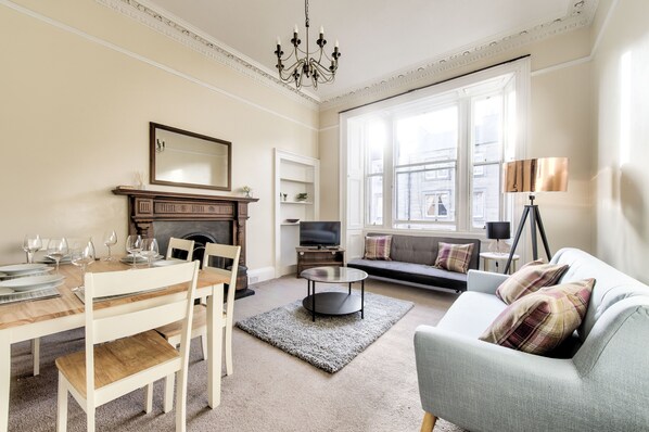 A living room with a dining table set, a sofa, a fireplace, and a television.