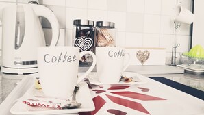 Dos tazas blancas de café con la palabra "Coffee" escrita en ellas, una tetera blanca y una máquina de café sobre una encimera de cocina.