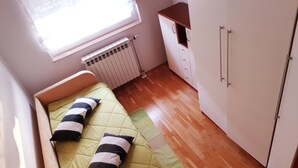 Una habitación pequeña con cama individual, ventana, radiador y una zona de kitchenette.
