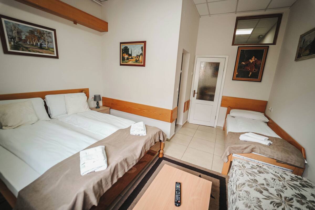 A hotel room with two beds, a small table, and a door leading to another room.