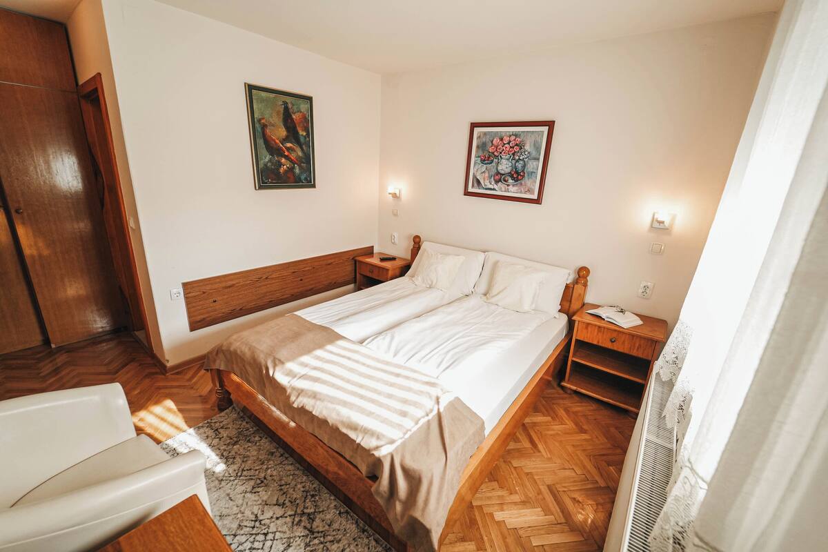 A bedroom with a wooden bed, a nightstand, a bedside table, and a chair.