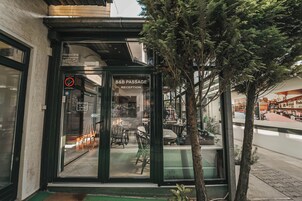 Entrada de restaurante com porta de vidro, mesas ao ar livre visíveis através da porta e uma árvore em frente.