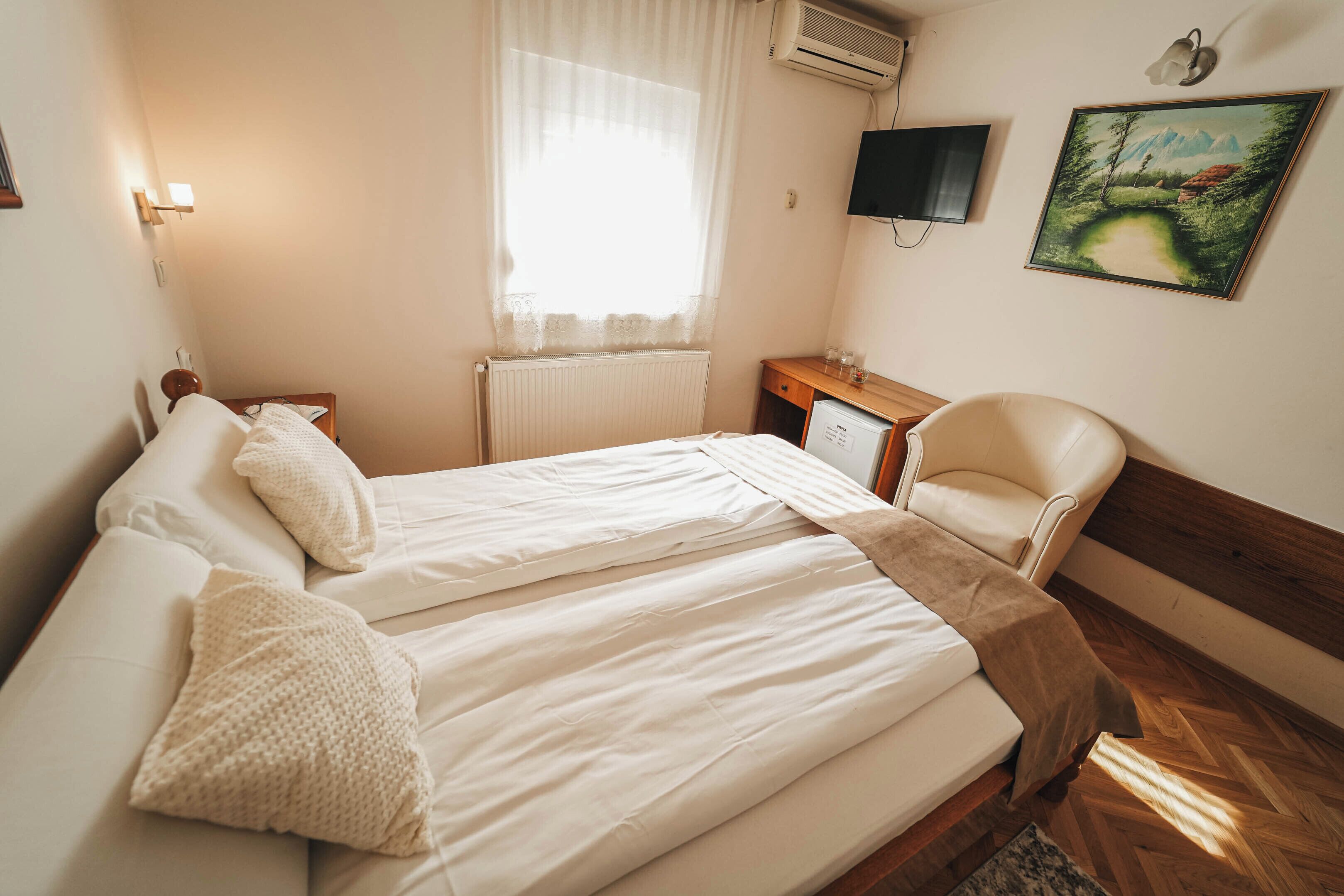 Un dormitorio con una cama, una silla, un escritorio, un televisor y un cuadro en la pared.
