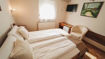 Un dormitorio con una cama, una silla, un escritorio, un televisor y un cuadro en la pared.
