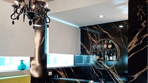 En moderne bar med væg i sort marmor, en gul polstret bænk og en lysekrone.