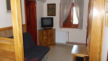 Una habitación con un sofá de madera, un televisor sobre un mueble de madera, una ventana con cortinas y un radiador.