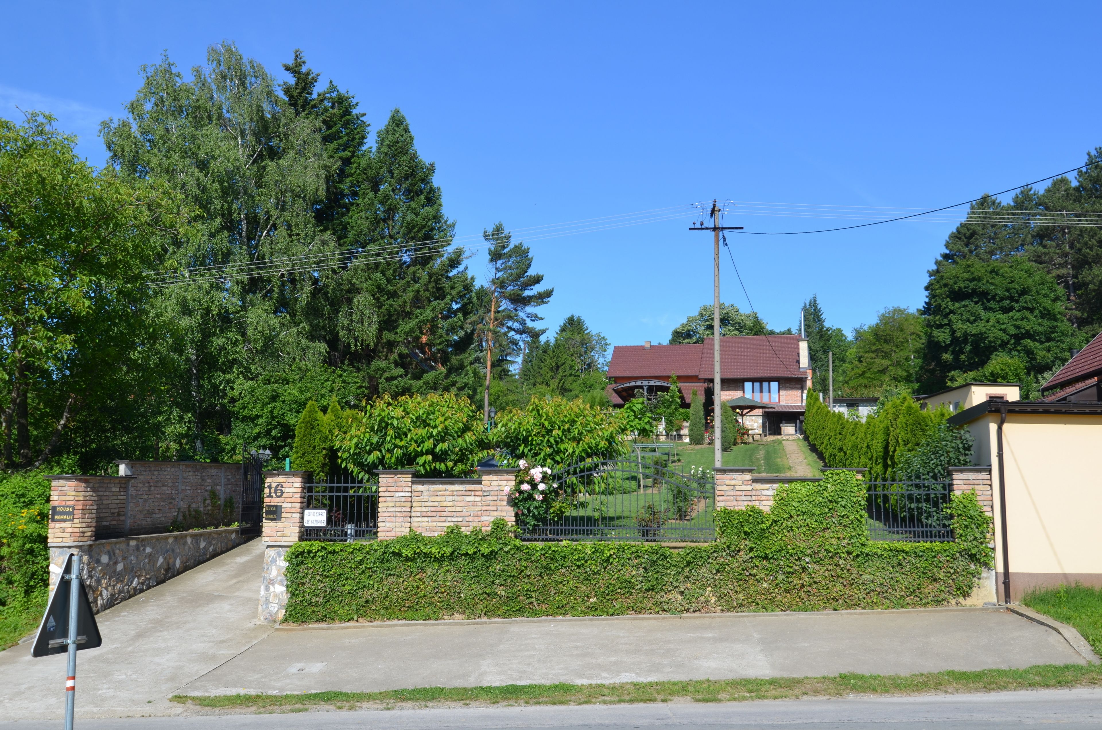 A gated residential area with a brick wall, a paved driveway, and a house with a red roof.