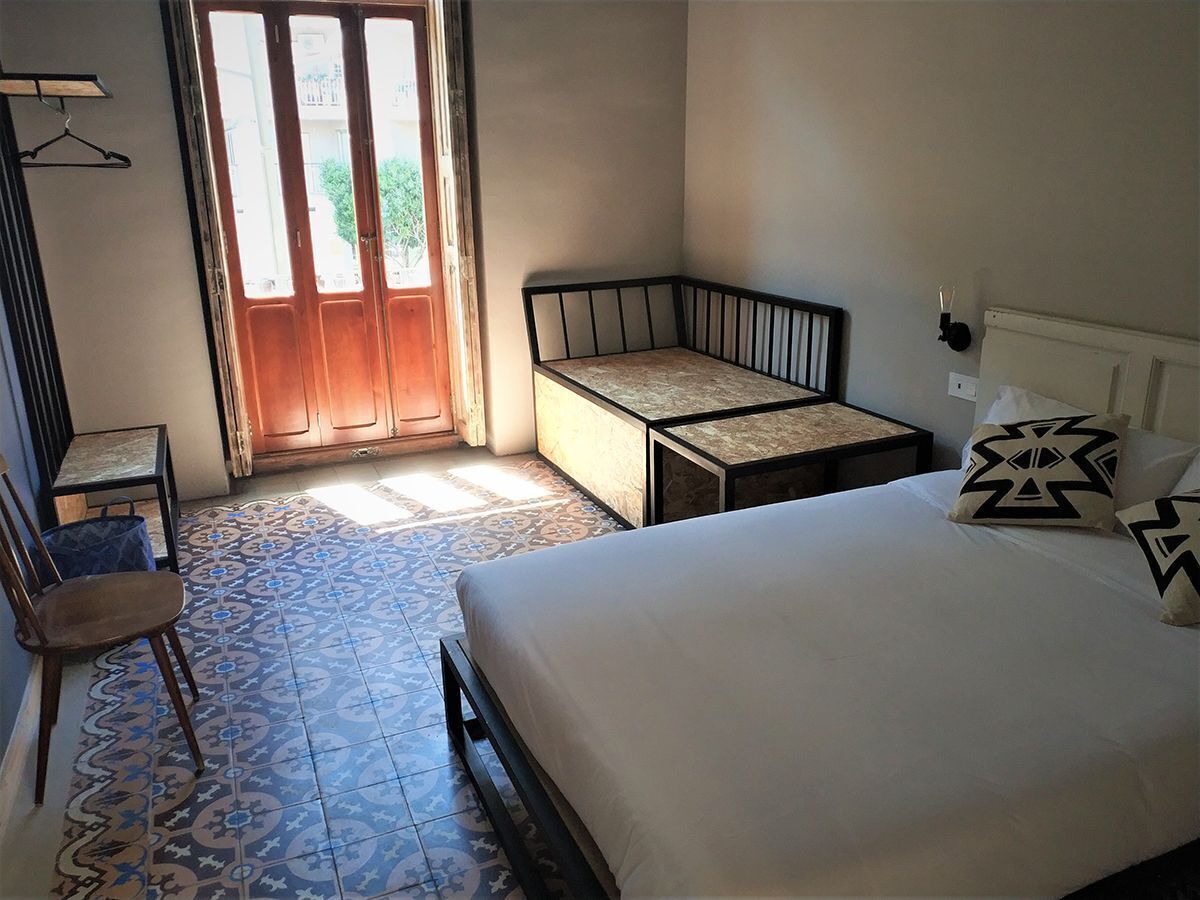 A bedroom with a bed, a chair, a small table, and a window with a view of greenery.