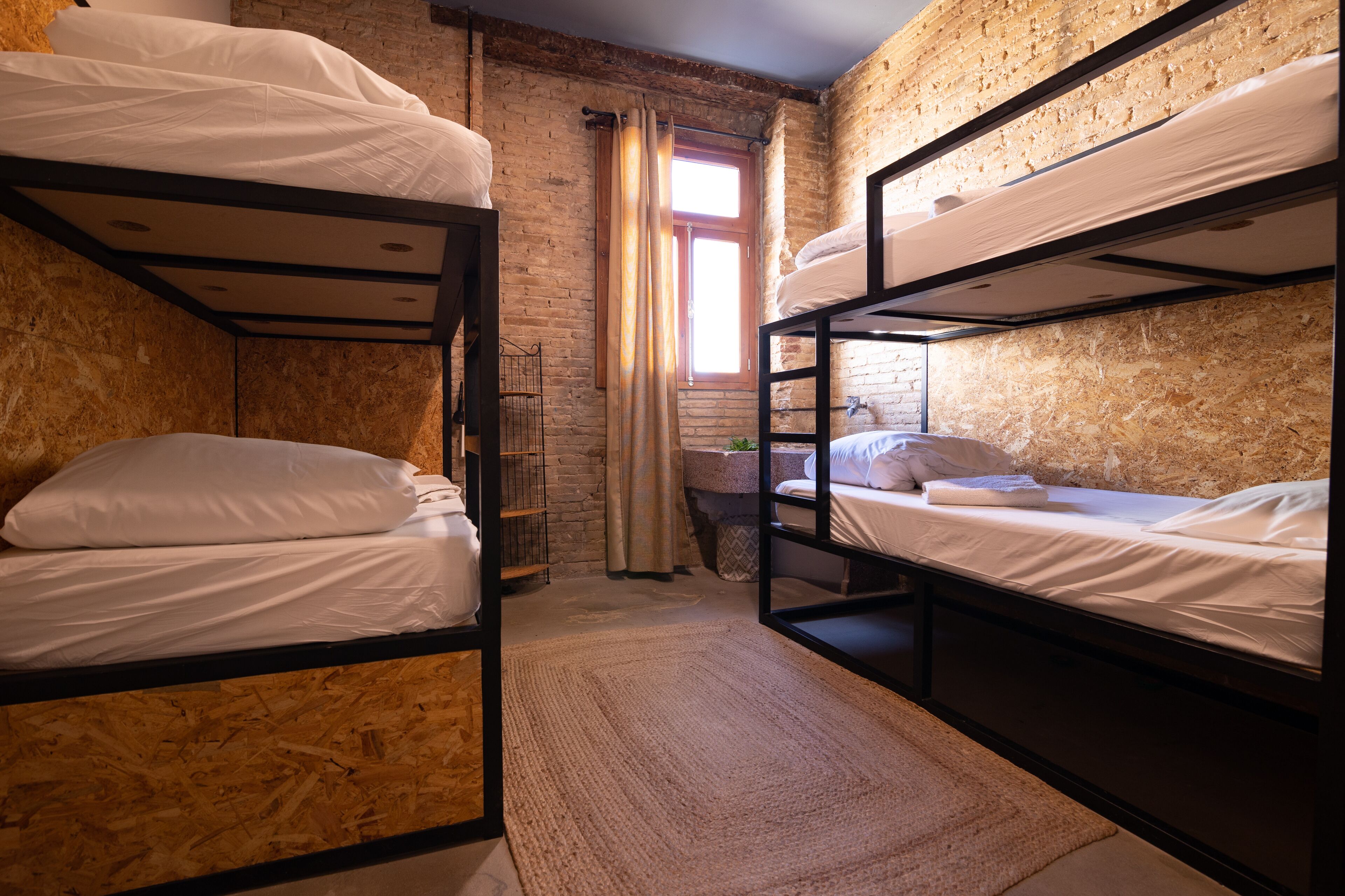 A room with bunk beds, a window with curtains, and a brick wall.