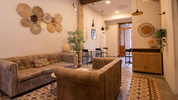 A living room with a sofa, armchair, and decorative wall art. There is a dining area in the background with a table and chairs. - BirdHouse Valencia (Valencia)