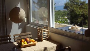 A room with a table set for breakfast, a basket of fruit, a wooden bench, and a view of the sea through a window. - In the center of Ancient Greece and Saronic sea (Corinthos)