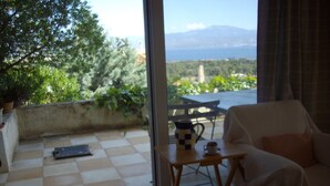 A room with a checkered floor, a white sofa, a small table with a coffee pot and cup, and a view of greenery and mountains through a glass door. - In the center of Ancient Greece and Saronic sea (Corinthos)