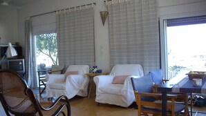 A room with two white armchairs, a wooden dining table, a wicker chair, and a television. - In the center of Ancient Greece and Saronic sea (Corinthos)