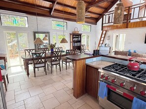 Uma cozinha com ilha central, cadeiras de madeira, fogão e mesa de jantar.