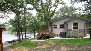 A lakeside cabin with a wooden staircase leading to a deck, surrounded by trees and a view of the lake. - Waterfront beauty with dock and fireplace! Check in Bay! New Hot Tub!! (Afton)