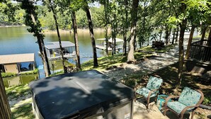 A hot tub with a cover, surrounded by trees and a lake view. - Waterfront beauty with dock and fireplace! Check in Bay! New Hot Tub!! (Afton)