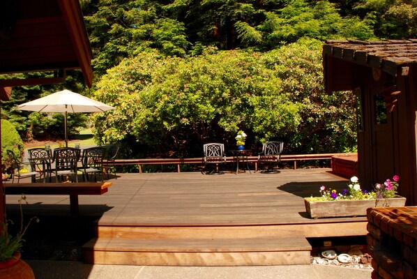 A wooden deck with outdoor furniture, surrounded by lush greenery and a wooden pergola.
