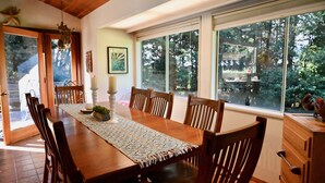 A dining area with a wooden table, chairs, a patterned runner, and a view of trees through large windows. - Beautiful Home in the Heart of the Majestic Redwoods.  Secluded on 10 acres. (Fort Bragg)
