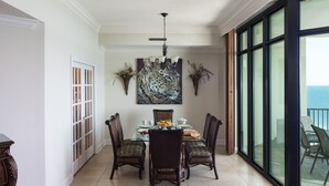 A dining area with a glass table, four chairs, a chandelier, and a large painting. - Beach Front, Spacious, Clean and Comfortable (Orange Beach)