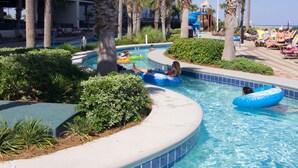 A swimming pool area with palm trees, lounge chairs, and a water slide. - Beach Front, Spacious, Clean and Comfortable (Orange Beach)