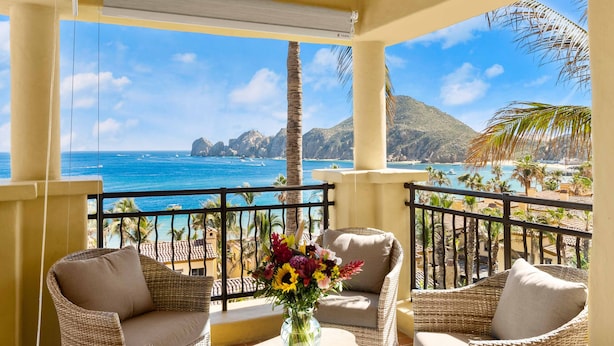 Un balcón con muebles de mimbre, un florero con flores y vistas al océano y a las montañas.