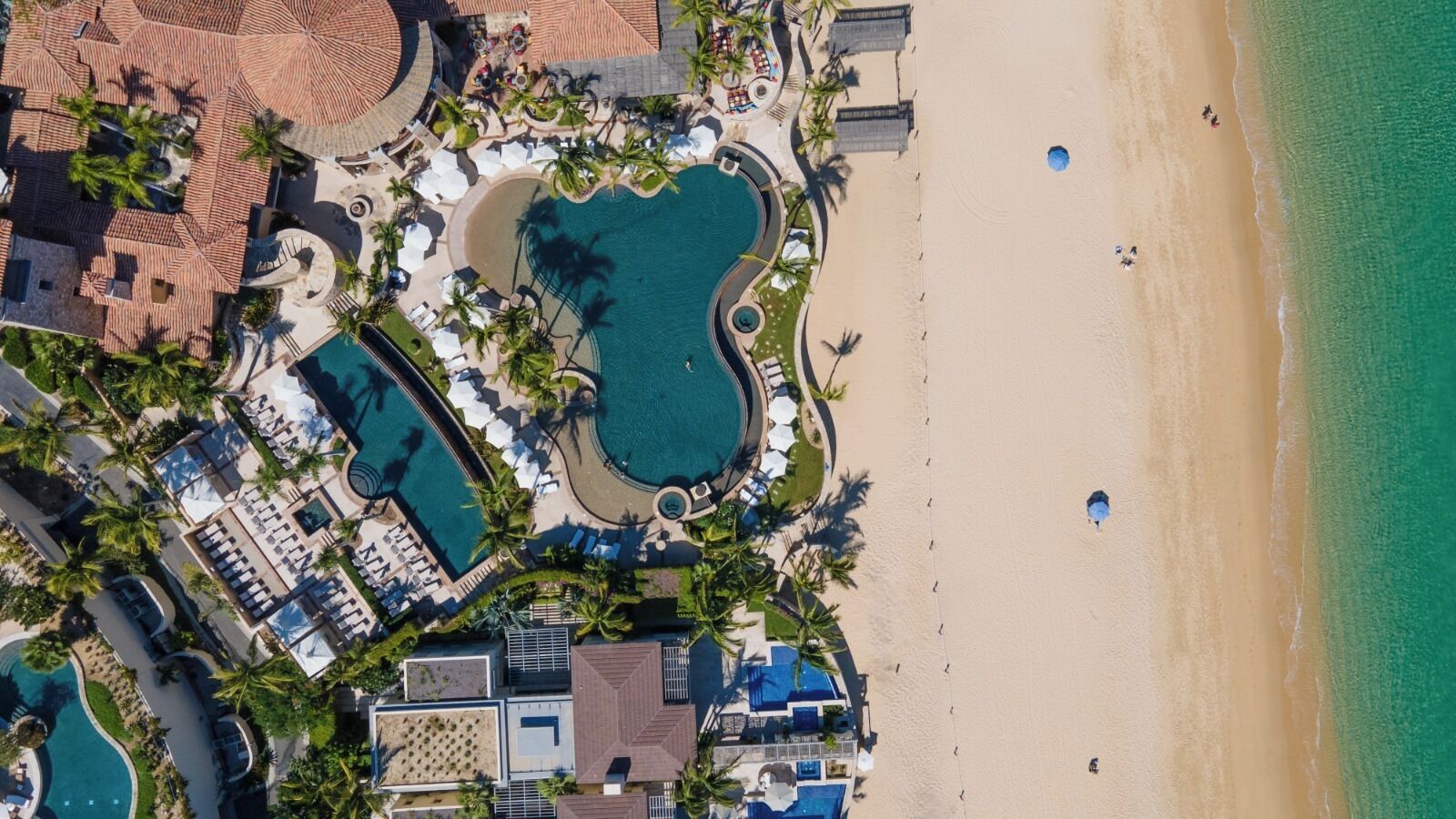 Eine Luftaufnahme eines Resorts mit mehreren Schwimmbecken, einem Strand und Palmen.