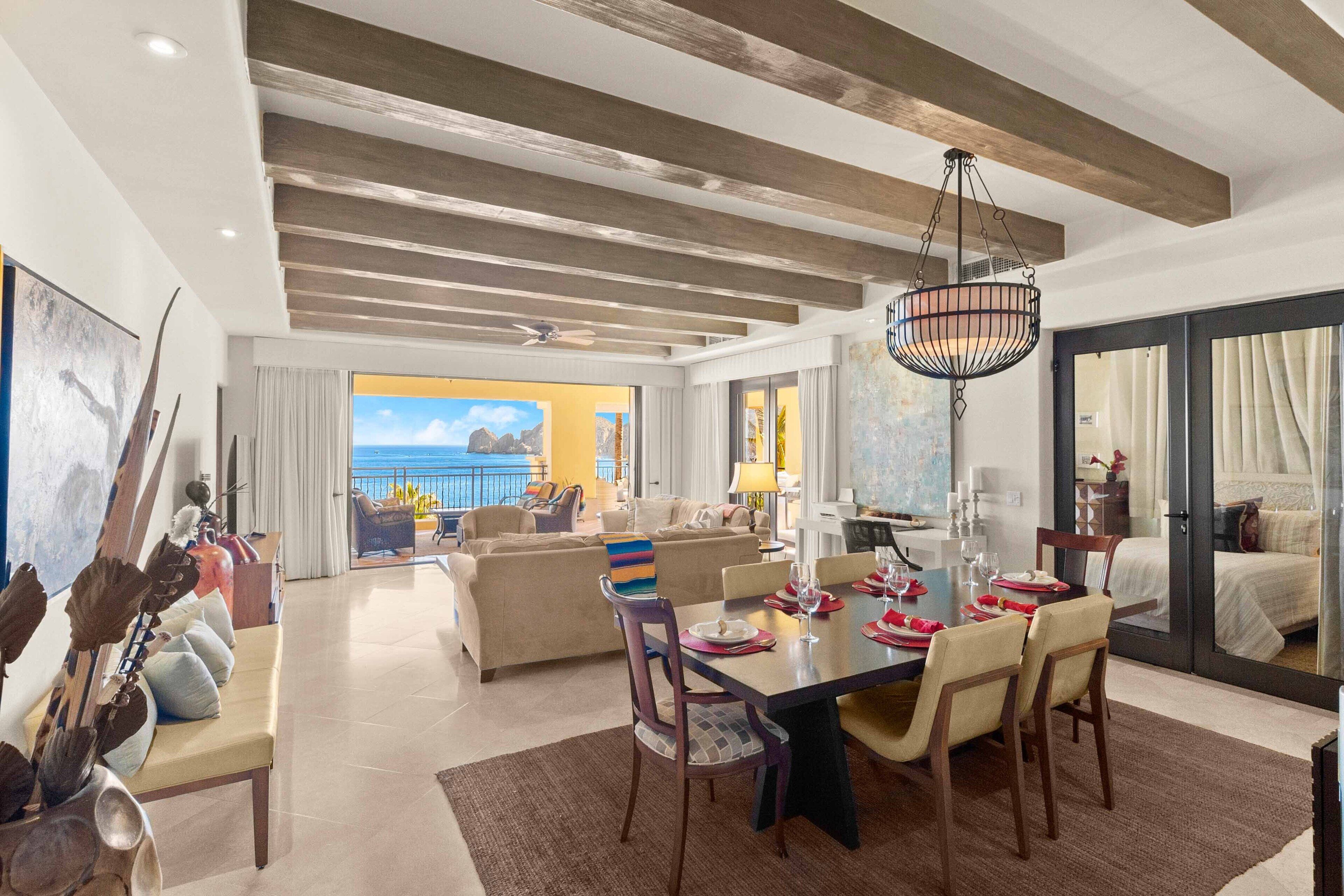 A spacious living area with a large dining table, comfortable seating, and a view of the sea.