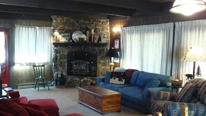 A cozy living room with a stone fireplace, a blue sofa, red armchairs, and a wooden coffee table. - Rushing Creek w/Mountain Views! Perfect Cabin for Family/Couples Getaways! (Nathrop)