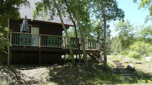 A wooden cabin with a deck, surrounded by trees and a grassy area. - Rushing Creek w/Mountain Views! Perfect Cabin for Family/Couples Getaways! (Nathrop)