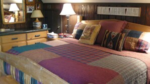 A cozy bedroom with a wooden headboard, a quilted bedspread, and a bedside table with a lamp. - Rushing Creek w/Mountain Views! Perfect Cabin for Family/Couples Getaways! (Nathrop)
