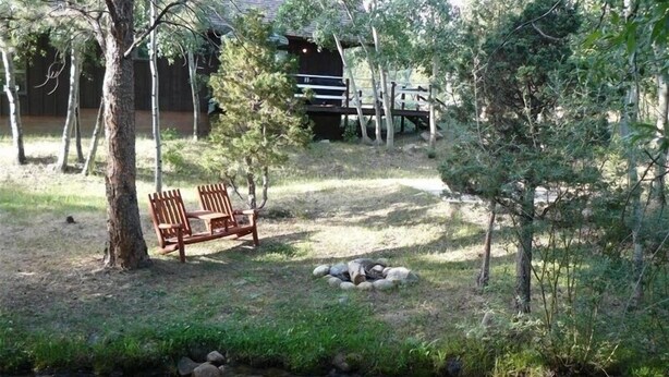 A serene outdoor area with a wooden bench, a small stream, and a rustic building in the background. - Rushing Creek w/Mountain Views! Perfect Cabin for Family/Couples Getaways! (Nathrop)