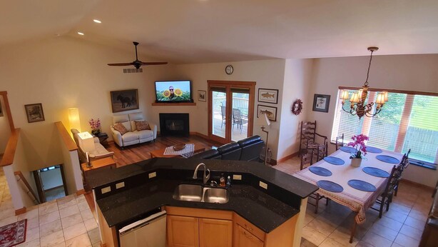 A spacious living area with a fireplace, a dining table with chairs, a kitchen with a sink, and a ceiling fan.