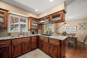 A kitchen with wooden cabinets, a granite countertop, a built-in stove, and a dining area with a table and chairs. - Downtown Coeur d'Alene Retreat w/ Pool Table & Fire Pit (Coeur d'Alene)