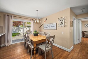 A dining area with a wooden table, chairs, a chandelier, and a view of the outdoors.