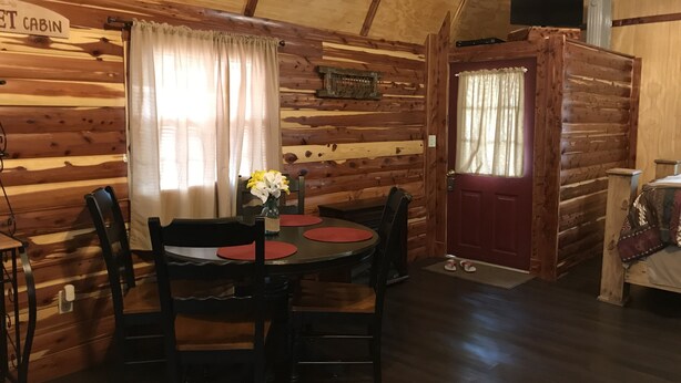 A cabin interior with a wooden interior, a dining table with chairs, a vase with flowers, and a red door. - Lovely secluded rustic cabin within waking distance of Rocky Top Winery . (Atwood)