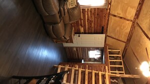 A wooden cabin interior with a brown leather sofa, a white door, and a staircase. - Lovely secluded rustic cabin within waking distance of Rocky Top Winery . (Atwood)