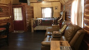 A log cabin room with a bed, a leather sofa, a wooden table, and a ceiling fan. - Lovely secluded rustic cabin within waking distance of Rocky Top Winery . (Atwood)