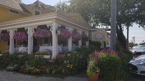 Ein gelbes Gebäude mit überdachter Veranda, weißen Säulen und hängenden Blumenkörben.