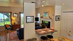 A modern kitchen with a fireplace, bar stools, and a dining table. - Great Price! Sunset Beach Cottage with Lovely garden, beach, and boat dock! (Nice)