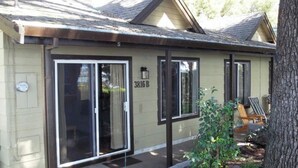 A single-story building with a beige exterior, large sliding glass doors, and a small porch with a chair. - Great Price! Sunset Beach Cottage with Lovely garden, beach, and boat dock! (Nice)
