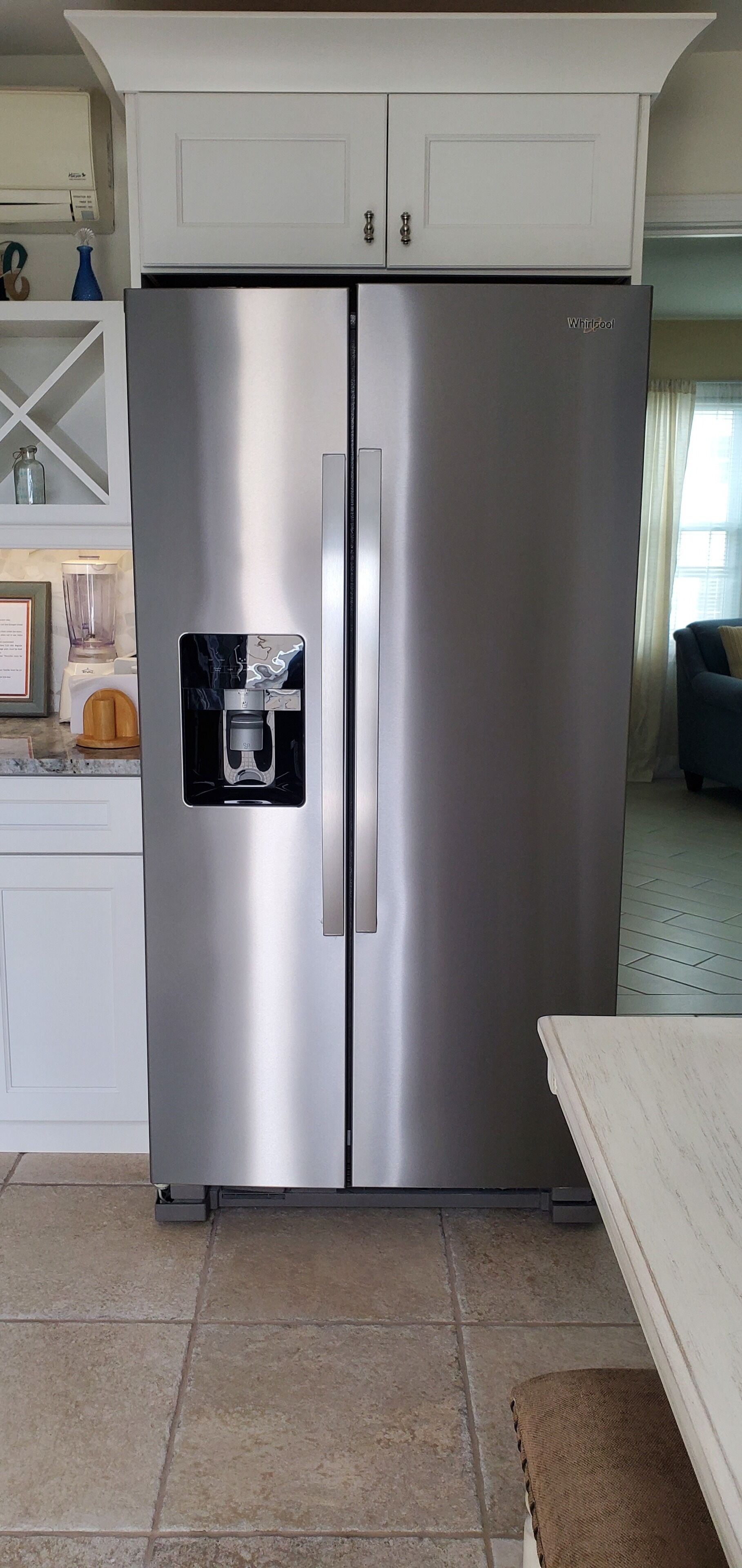 A stainless steel Whirlpool refrigerator with a built-in ice maker, white cabinetry, and a tiled floor.