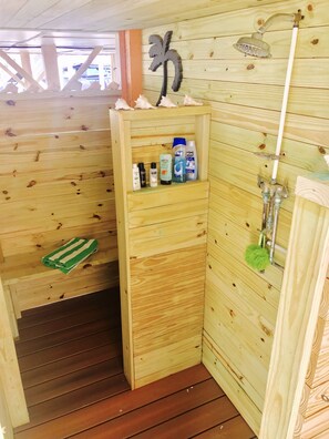 Una sauna de fusta amb una prestatgeria que conté productes de cura personal, un vàter de dutxa i una tovallola verda.