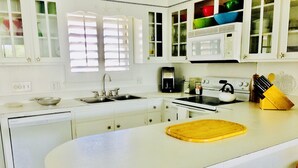 A kitchen with white cabinets, a black and white checkered floor, a sink, a stove, and a wooden cutting board. - The Sea Palm, A Coastal Cottage Steps From The Beach!!! (Sunset Beach)