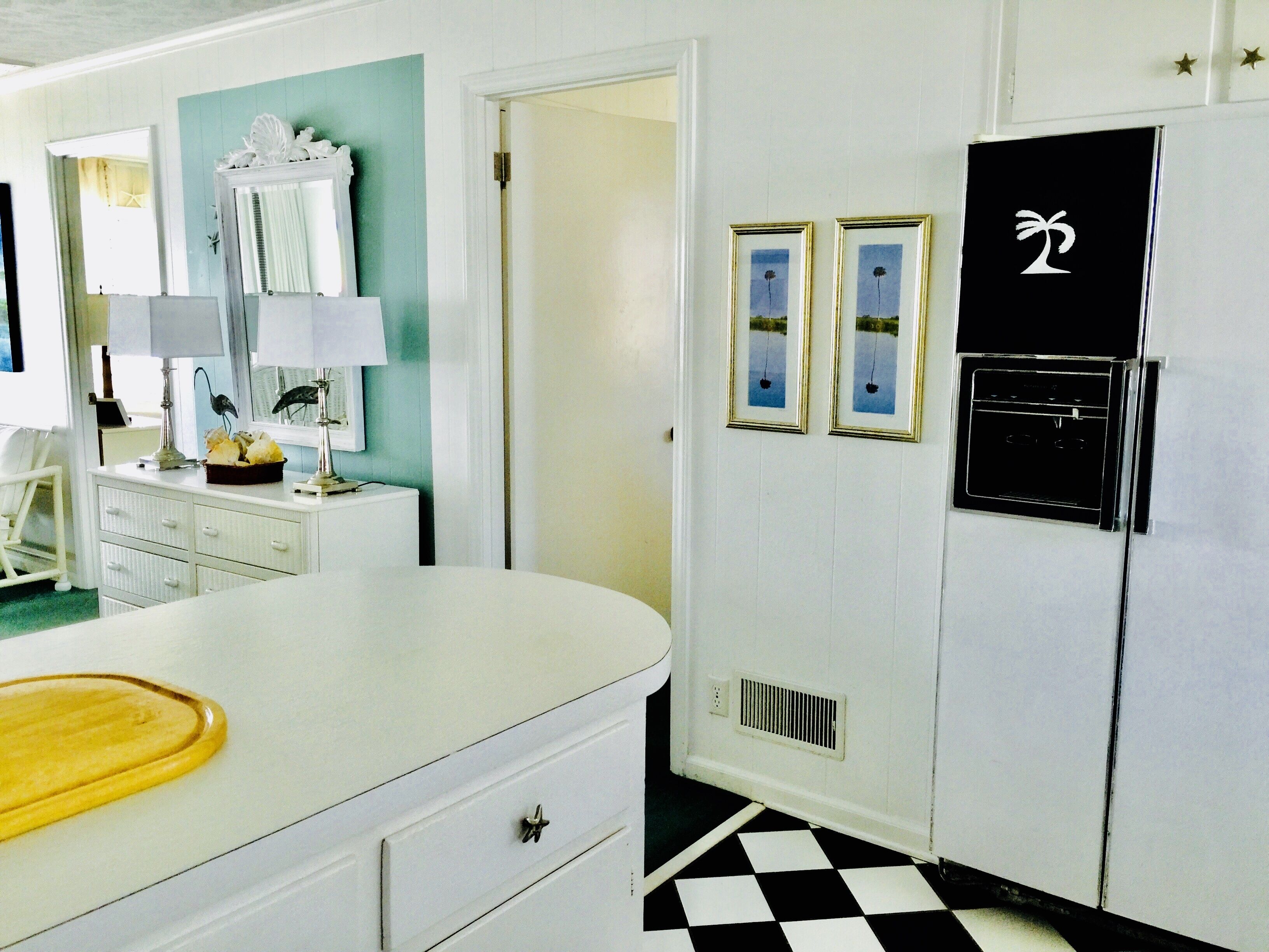 A kitchen with a white countertop, a refrigerator, and a black and white checkered floor.