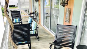A covered porch with wooden flooring, black metal chairs with striped cushions, and a rope decoration. - The Sea Palm, A Coastal Cottage Steps From The Beach!!! (Sunset Beach)