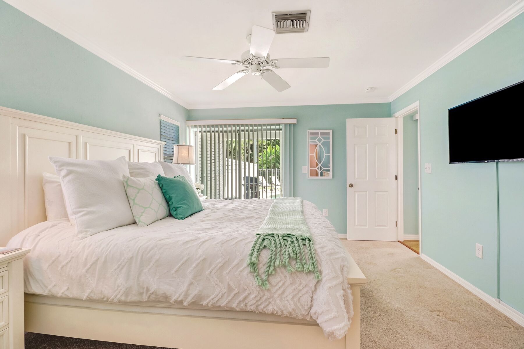 A bedroom with a bed, a ceiling fan, a TV, and a window with blinds.